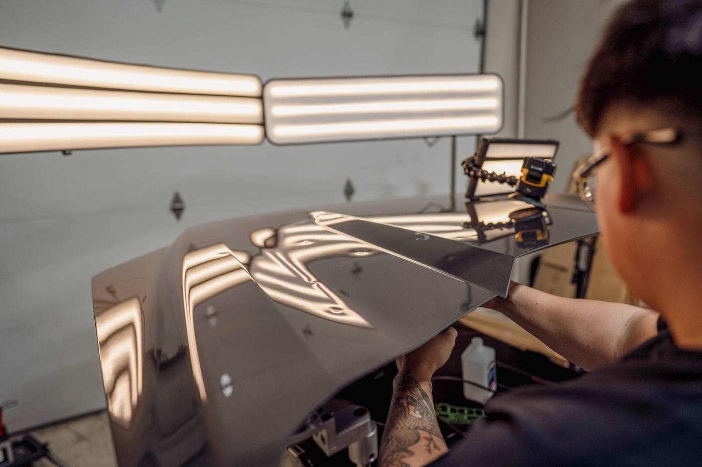 Body panel held under light bars so hail dents can be read.